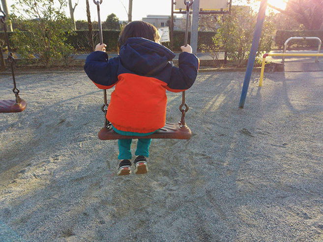 子どもがブランコに乗っている後ろ姿の画像
