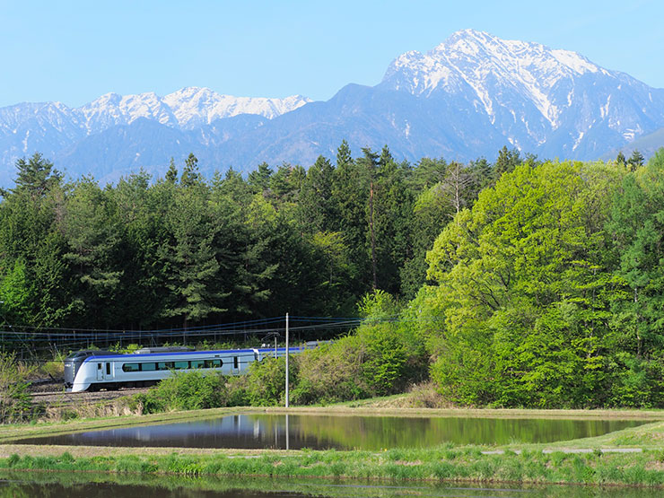 OM SYSTEM OM-D E-M1 MarkⅡ・M.ZUIKO DIGITAL ED 40-150mm F2.8 PRO・50mm（35mm判換算100mm）で撮影した新緑の季節に斐駒ヶ岳と水田の間を走る特急「あずさ」　の画像