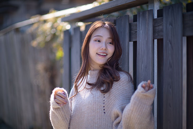 ニコン D850・AF-S NIKKOR 85mm f/1.4Gで撮影した木の塀の前に立つ女性の画像