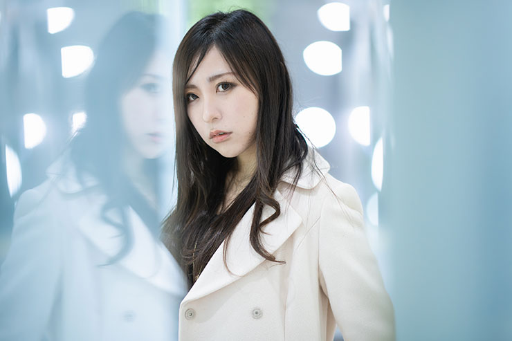 ニコン D850・AF-S NIKKOR 105mm f/1.4E EDで撮影したライトが映るガラスの前に立つ女性の画像