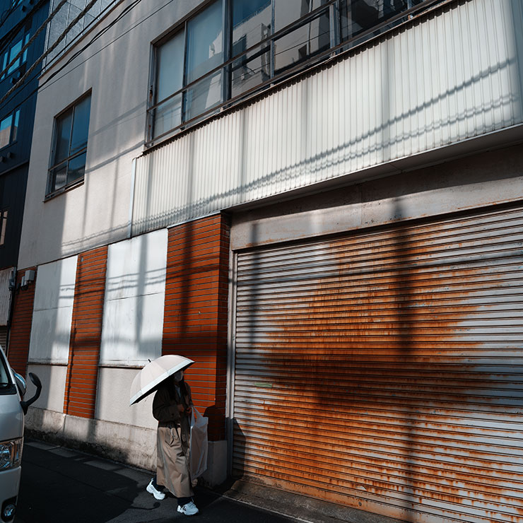 シグマfp L・シグマ23mm F1.4 DC DN | Contemporaryで撮影した建物の横を歩く日傘をさした女性の画像