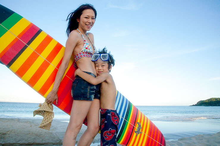 対角線構図で撮影したサーフィンを持った母親と母親に抱き着く男の子の画像