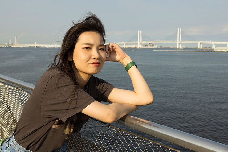 海沿いのフェンスに肘をつく女性の画像