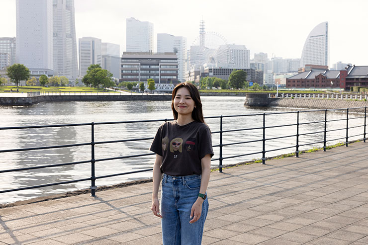 ストロボなしで撮影したビルや川を背景にポーズをとる女性の画像