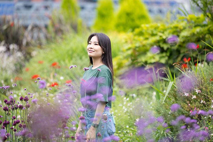 花や緑の植物の中に立っている女性の画像