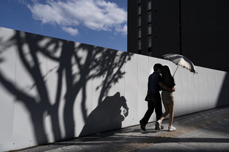 Nikon NIKKOR Z 24-70mm f/2.8 S II作例：工事現場の白い壁の前を通る肩を寄せ合う男女